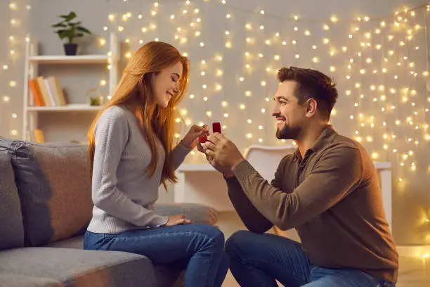 Will you marry me. Couple making love promise to each other on cozy evening at home. Happy woman getting romantic marriage proposal. Young man proposing to girlfriend and giving her engagement ring