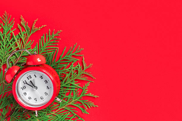istock Alarm clock  with tree branches on red paper background. 5 minutes before the New Year. Creative greeting card. 1356421694