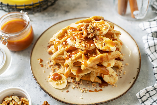 Banana waffles with walnuts and salted caramel in a plate on a culinary background