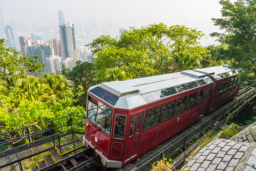 The iconic ruby cable cars of the Peak Tram climbing through the green hillside of Victoria Peak above the crowded skyscraper cityscape of Hong Kong, China.