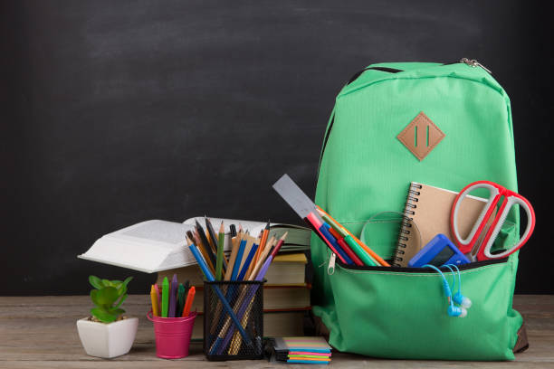 istock Education concept - school backpack with books and other supplies, blackboard background 1356422731