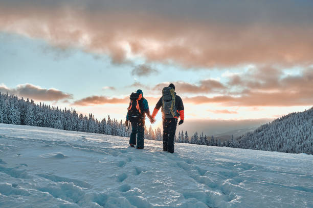 descanse nas montanhas. casal de família de mãos dadas e caminhando nas montanhas de pinheiros nevadas ao pôr do sol. o conceito de recreação e turismo no inverno. - skiing winter snow winter sport - fotografias e filmes do acervo