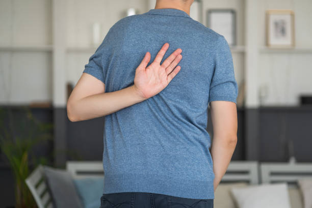 Pain between the shoulder blades, man suffering from backache at home