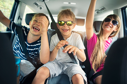 Three kids aged 11 and 7 are having fun in car during a road trip. The kids are wearing shades on and having a lot of fun during road trip. \nSunny summer day in Andalusia, Spain.