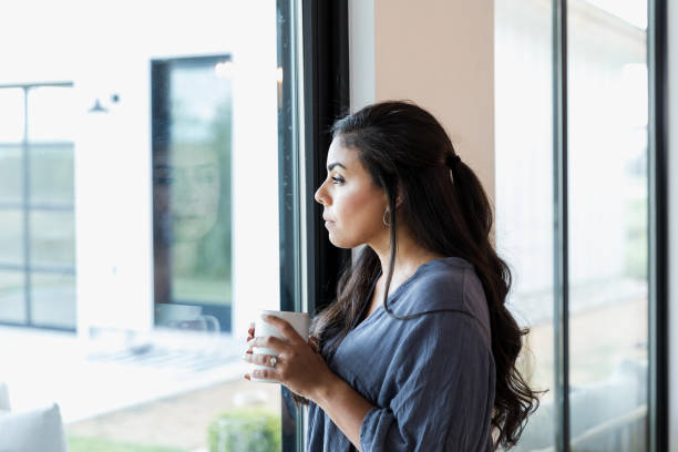 istock Sad woman looks through window 1356429549