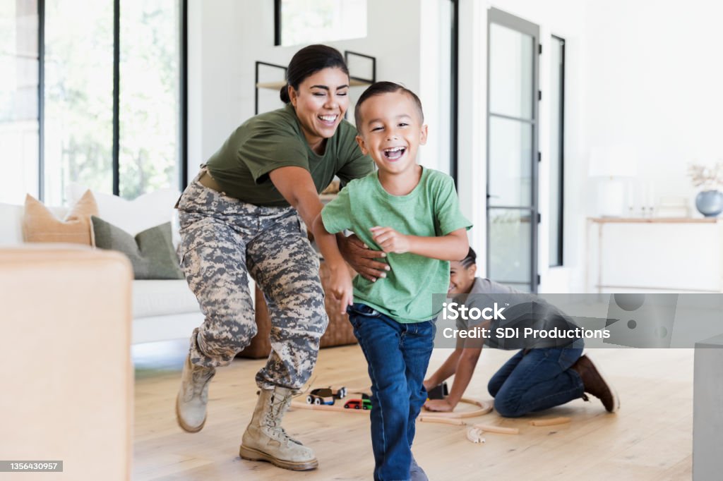 After work, female soldier chases son in house While the preteen boy sets up the wooden train set on the living room floor, the female soldier chases the elementary age boy through the house.  Everybody is smiling and happy. Family Stock Photo