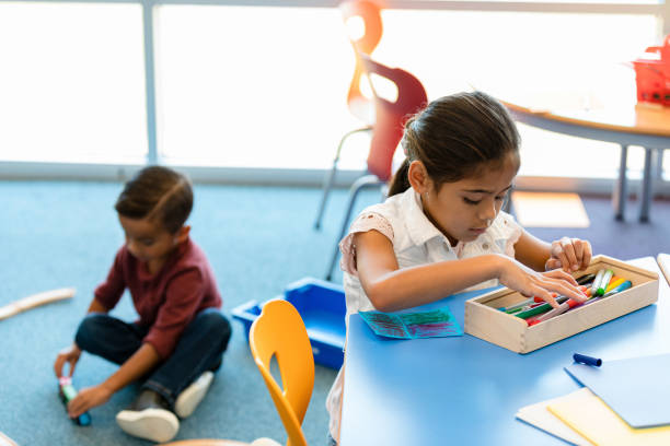 istock Young girl colors while male classmate plays with trains on floor 1356433413