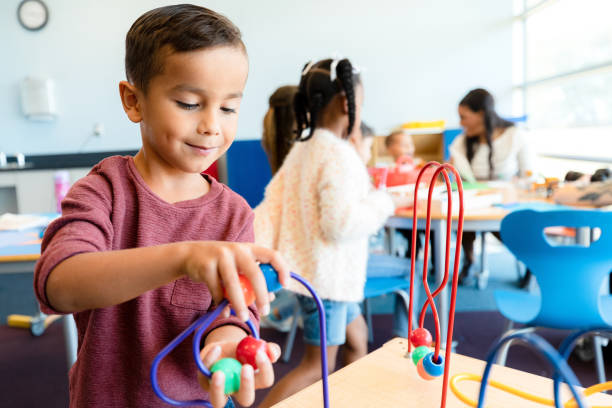 istock Boy focuses on bead puzzle while classmates play in background 1356433445