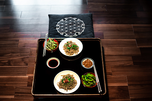 Traditional Japanese restaurant ryokan kaiseki with food dish of boiled edamame, natto and soy sauce on plate by chopsticks and soba buckwheat noodles above high angle view nobody