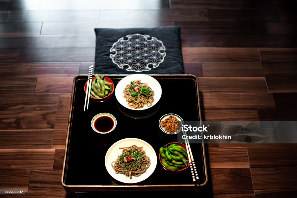 Traditional Japanese restaurant ryokan kaiseki with food dish of boiled edamame, natto and soy sauce on plate by chopsticks and soba buckwheat noodles above high angle view nobody Shojin Ryori Stock Photo