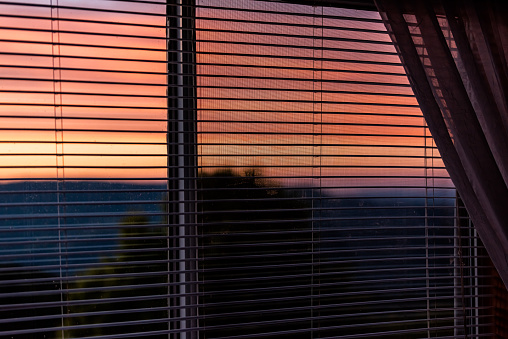 Sunset dusk twilight in Sugar Mountain house apartment with view through window blinds and vibrant red orange color sky in North Carolina Blue Ridge Appalachias
