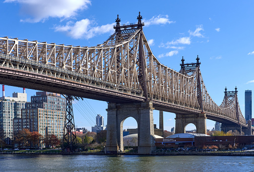New York, NY - November 23, 2021: The Ed Koch Queensboro Bridge (1909) passing over the East River and Roosevelt Island. Apartment buildings and inflatable tennis bubbles can be seen on a clear autumn day.