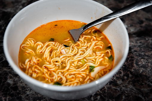 Macro closeup of one spicy red ramen noodle instant soup in bowl with fork as Japanese asian meal with texture of pasta and green onion toppings