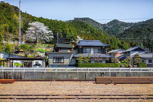 Gero Onsen, Japan village houses view from train in Gifu prefecture with railroad tracks and mountain view in spring springtime during day with cherry blossom flowers blooming