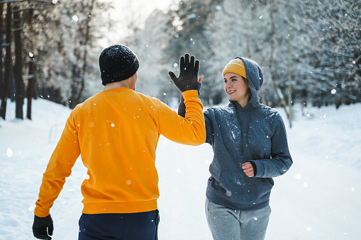 Two joggers greeting each other with a high five gesture during winter workout outside