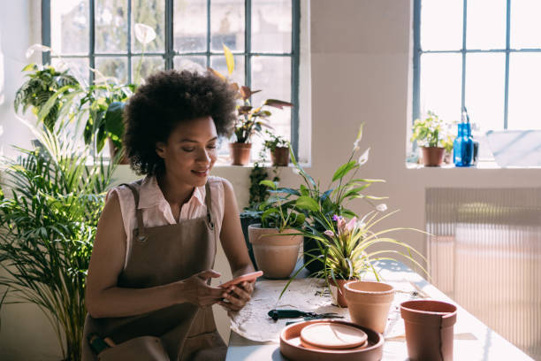 istock Smiling Female Florist Sitting in her Workshop and Using Mobile Phone 1356437539