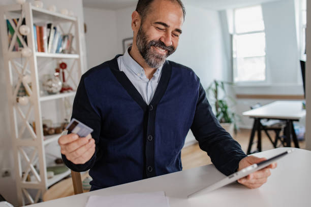 istock Mature man holding a credit while doing online shopping 1356440258