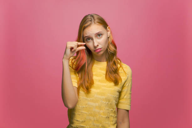 fille déçue montrant une petite taille avec pitié sur fond de studio rose. jeune femme montrant la mesure avec les doigts - low scale magnification photos et images de collection