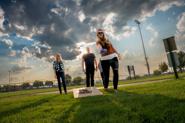 młoda czteroosobowa rodzina z dwiema córkami ciesząca się grą w kukurydzianą dziurę lub torby w parku w słoneczne letnie popołudnie w parku - cornhole leisure games outdoors color image zdjęcia i obrazy z banku zdjęć