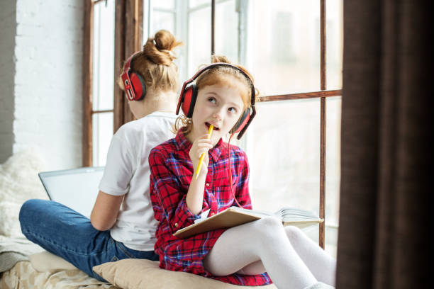 dwie siostry uczą się w domu. dzieci ze słuchawkami słuchające audiobooka. - window sill audio zdjęcia i obrazy z banku zdjęć