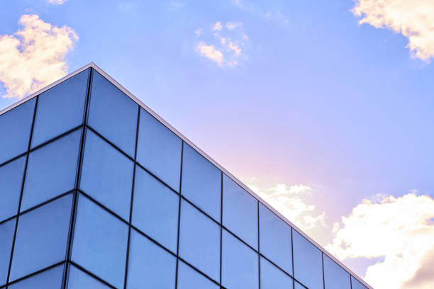 maison d’affaires moderne avec revêtement de façade en verre ou grandes fenêtres pleines de panneaux. bâtiment de vente au détail avec mur-rideau entièrement vitré extérieur à ciel bleu. immobilier urbain. architecture de bureau de centre commer - apartment window sky sun photos et images de collection