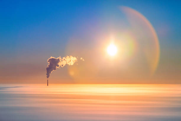 Smoke from high pipe of power station above the clouds, aerial view. Rising smoke from a high chimney of a thermal power plant over a low layer of temperature inversion which is lit by low winter sun.