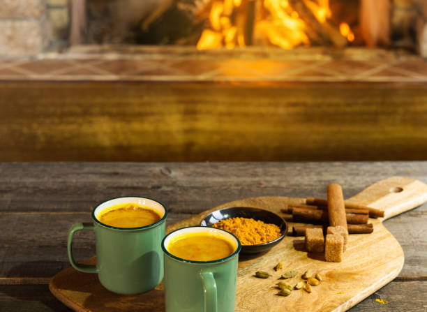 Golden latte milk made with turmeric and spices before cozy fireplace.