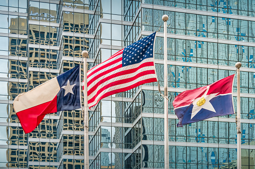 Flags of USA, Texas and Dallas fluttering in the wind with an office building in the background in downtown Dallas, Texas, USA.