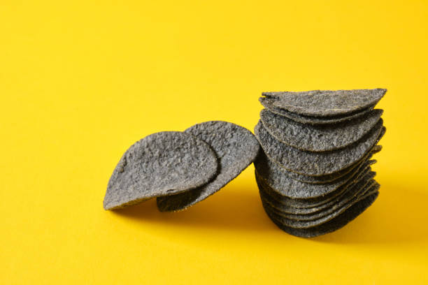 istock Black potato chips on yellow background. Black chips with activated charcoal and red pepper. 1356449764