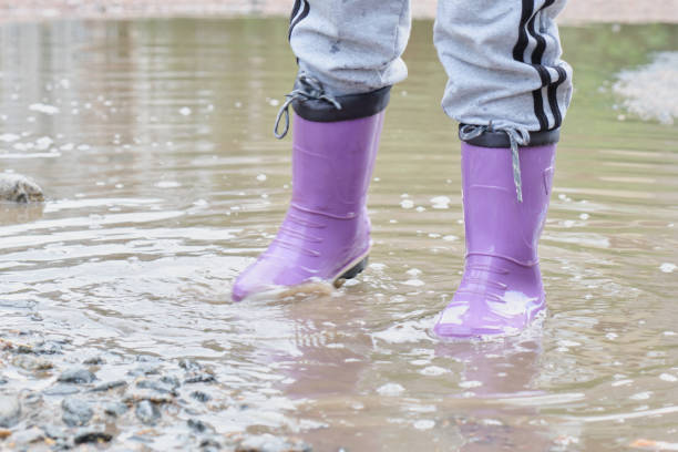 istock kid wearing lilac rain boots. Child iis jumping in a puddle. outdoors fun. 1356450594