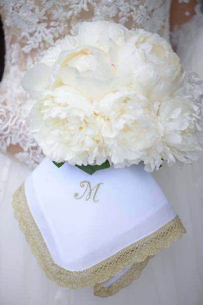 bride holding an exquisite white peonies wedding bouquet and an embroidered linnen napkin monogrammed with letter m - letter m alphabet color image flower imagens e fotografias de stock