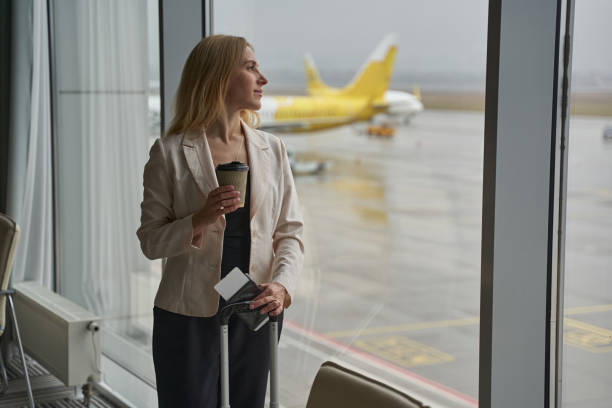 istock Woman drinking coffee while standing with luggage in airport terminal 1356455105