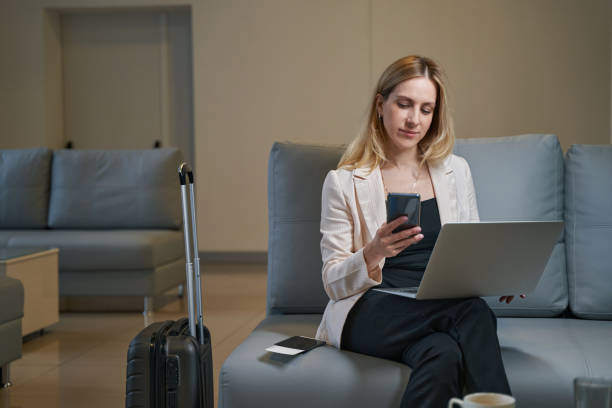istock Young lady dialing number on smartphone in hotel lobby 1356455111