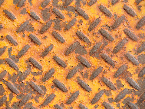 Close up of a rusty metal diamond plate background with yellow paint on it.