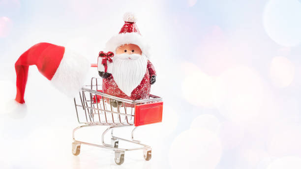 istock Gifts, spruce branches, red decorations on a white background.Decorative Santa's toy for a Christmas tree in a supermarket trolley on a light background with a Santa hat on a trolley. 1356462977