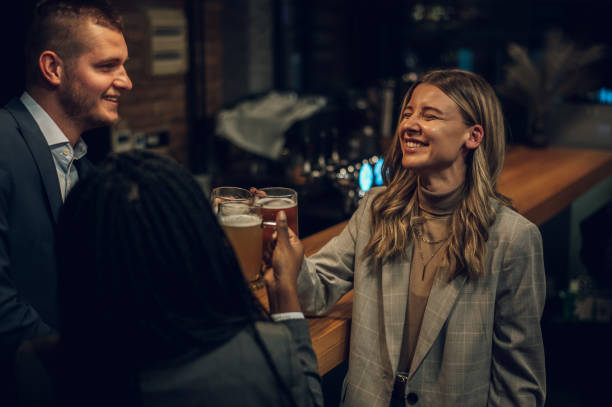 colegas alegres bebiendo cerveza en el bar juntos después del trabajo - afterwork business fotografías e imágenes de stock