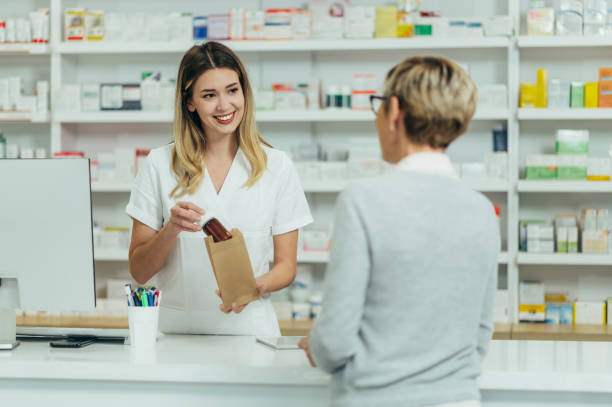 farmaceutka sprzedająca leki w aptece starszej klientce - pharmacist mature adult smiling senior adult zdjęcia i obrazy z banku zdjęć