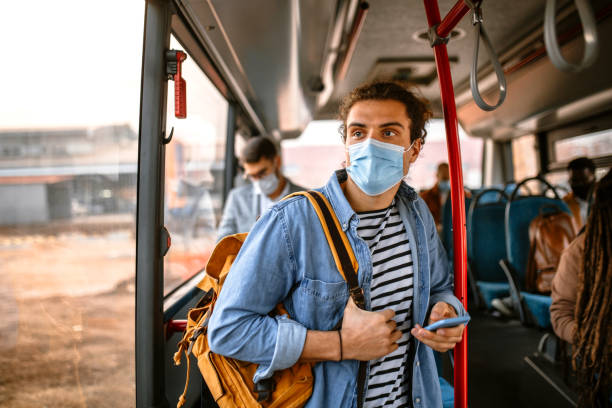 young man riding in bus wearing face mask - bus riding public transportation businessman imagens e fotografias de stock