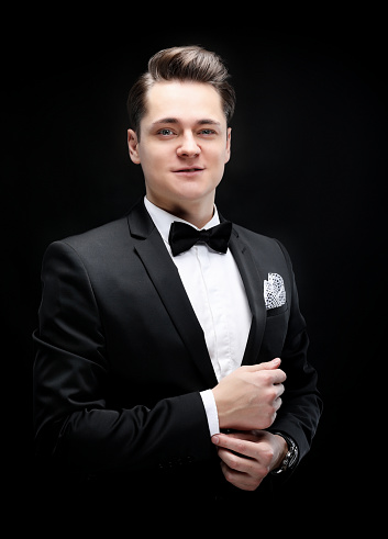 Portrait of handsome stylish man in elegant black suit over black background