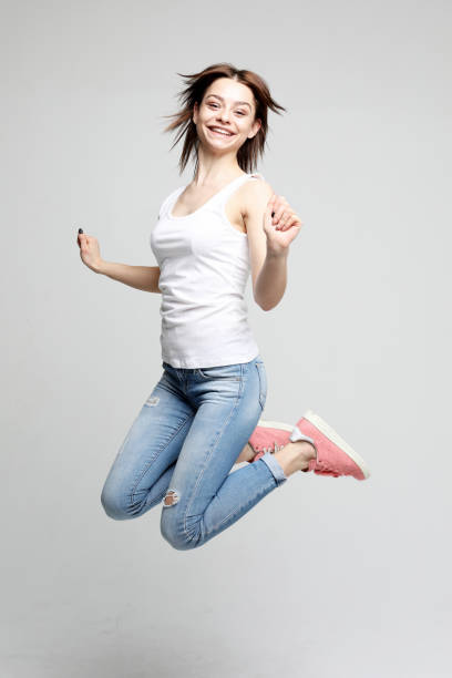istock smiling young woman jumping in air over white background 1356485020