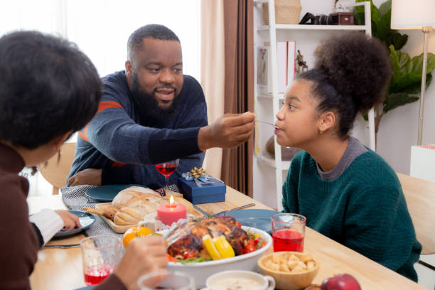 joyeux père de famille africaine nourrissant de la nourriture avec sa fille au dîner le jour de la veille de thanksgiving à la maison, père et mère et enfants fête de noël et du nouvel an en vacances. - new years day new years eve new year ethnic photos et images de collection