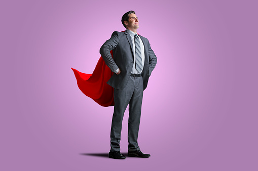 A  businessman wearing a red cape isolated on a purple background.