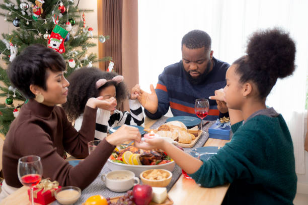 幸せなアフリカの家族は一緒に感謝祭の前夜の日に手をつないで夕食を祈ります, メリークリスマス, 食卓のお祝い, 家族の関係, 屋内, 新年とクリスマス. - new years day new years eve new year ethnic ストックフォトと画像