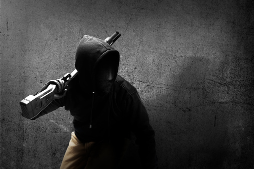 Criminal man in a hidden mask holding the shotgun with black wall background