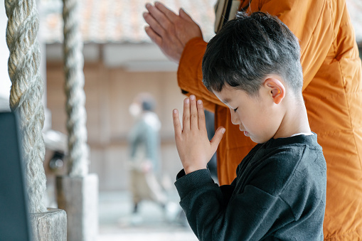 Young boy praying with his grandfather at a Japanese temple. Okayama, Japan