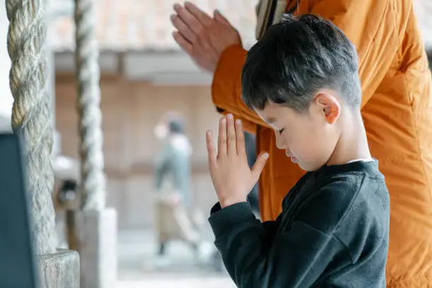 Photo of Young boy praying with his grandfather at a Japanese temple