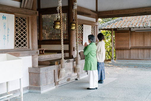 Senior woman and her adult daughter praying together at a temple. Okayama, Japan