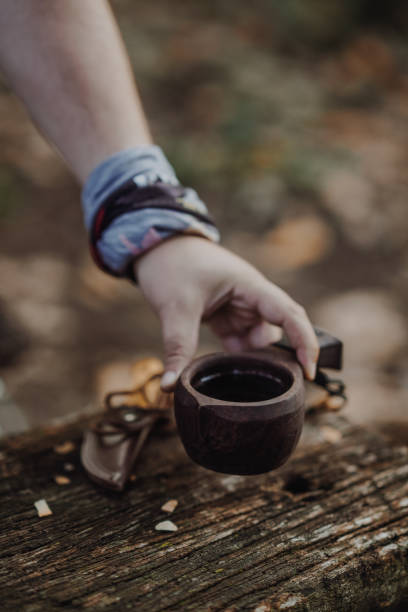 Bushcraft pours water from a bottle into a wood mug.