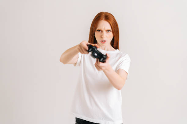 istock Studio portrait of serious young woman playing video game with controller looking at camera on white isolated background. 1356502794
