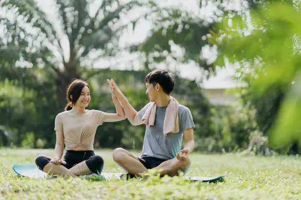 Full length shot of a young Asian couple doing yoga at outdoor public park.